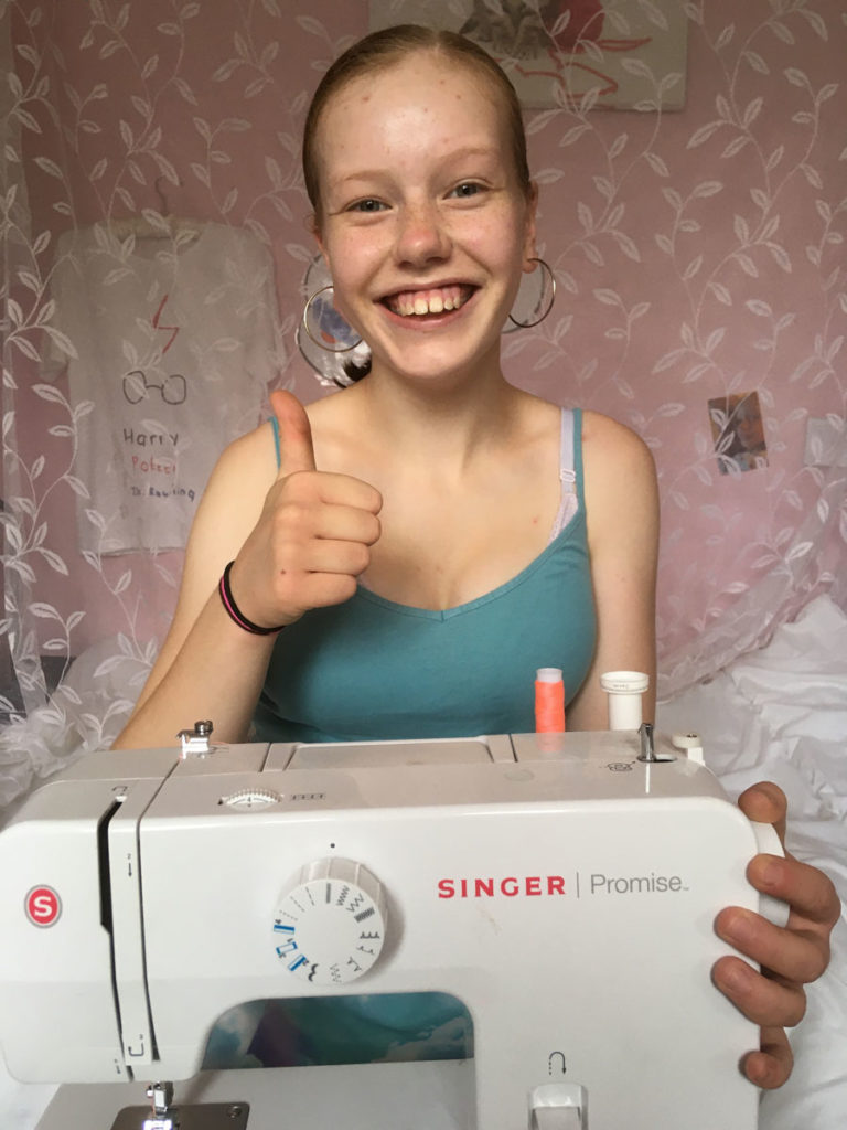 Young person giving a thumbs up and smiling with a sewing machine